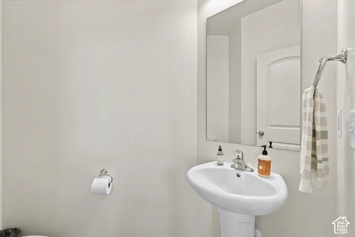 White pedestal sink with a chrome single-handle faucet, large frameless wall mirror, and chrome towel hardware