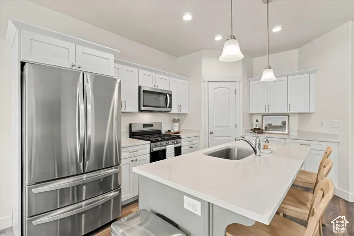 Kitchen featuring white shaker-style cabinetry, stainless steel appliances, a central island with a solid-surface countertop, an undermount sink, and recessed lighting with pendant fixtures