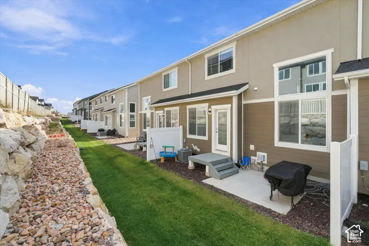 Exterior facade featuring multi-tonal horizontal siding, large picture windows, concrete patio, privacy partition, and tiered stone retaining wall