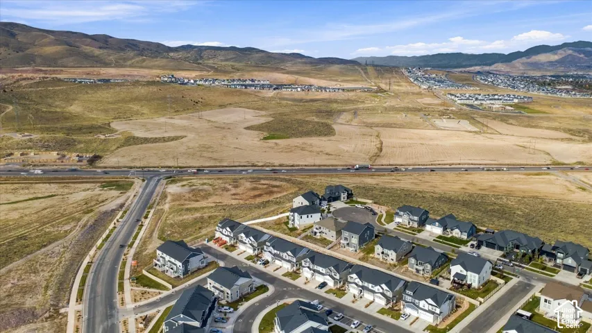 Aerial perspective of residential community featuring multi-level dwellings with pitched roofs, paved streets, and expansive mountain terrain backdrop