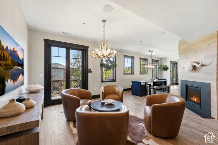 Open-concept interior featuring wood-finish flooring, a floor-to-ceiling wood-paneled fireplace with a linear insert, multi-light chandeliers, and glass-paneled exterior doors with dark casing