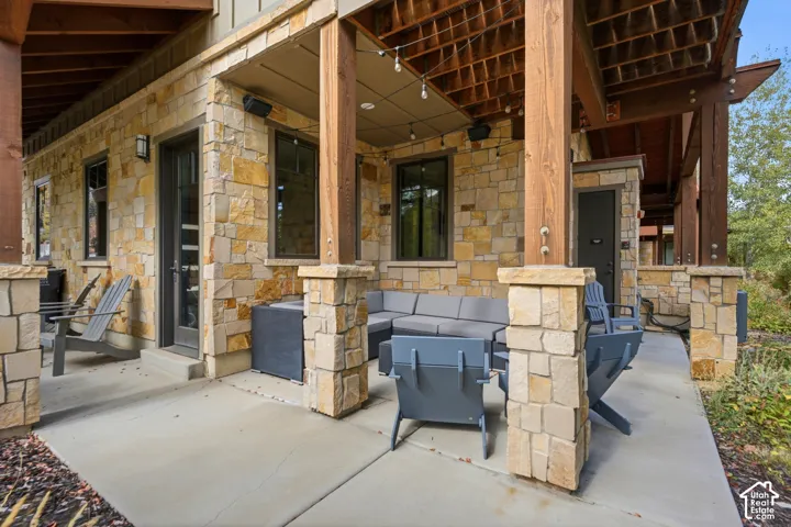 Covered patio featuring stone exterior cladding, concrete flooring, exposed timber support beams, and built-in recessed ceiling lighting
