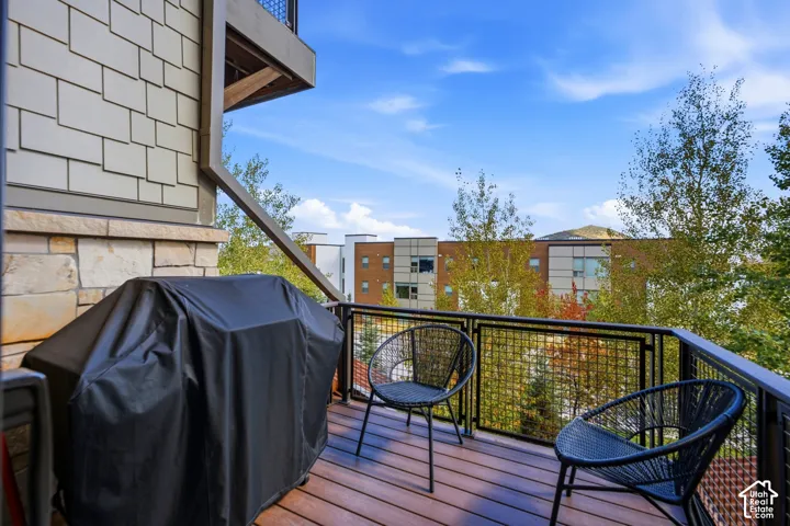 Private balcony featuring wood-finish decking, black metal grid railings, stone veneer exterior accents, and shingle siding