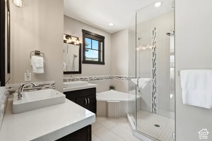 Bathroom featuring dual white rectangular vessel sinks, dark cabinetry, a quartz countertop, a corner soaking tub, and a glass-enclosed shower with mosaic tile accents