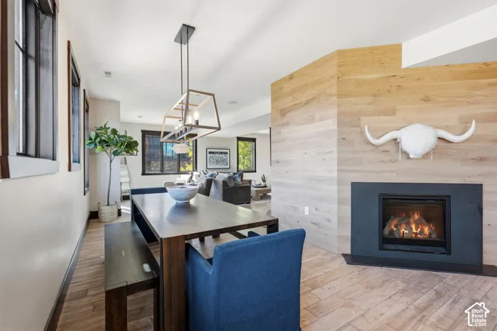 Gas fireplace with a dark surround, wood-plank accent wall, linear multi-light pendant fixture, and wood-finish flooring
