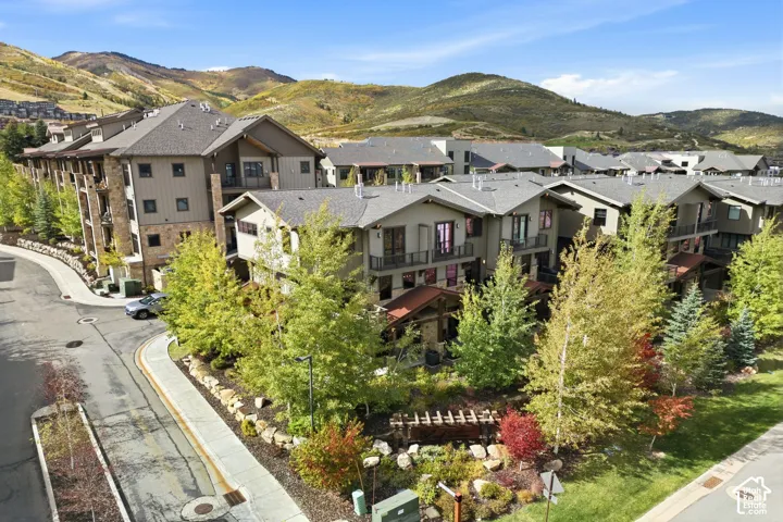 Multi-level exterior featuring wood and stone facade elements, private balconies with metal railings, a wooden pergola, professional hardscaping, and a mountainous backdrop