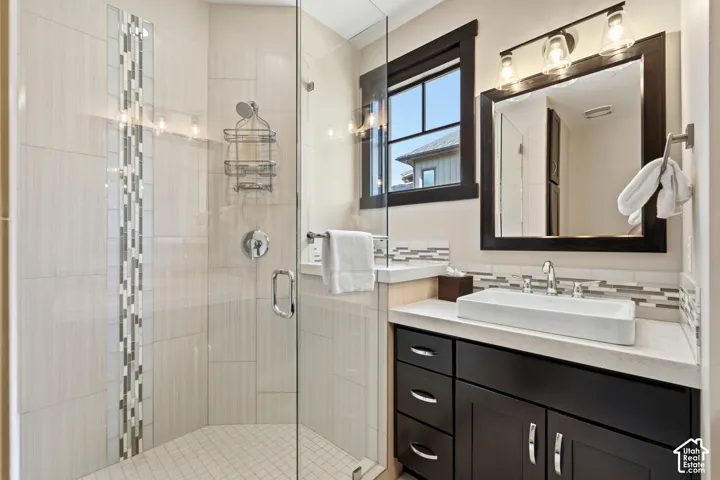Bathroom featuring a walk-in shower with glass enclosure and decorative tile inlay, stone-composite countertop with vessel sink, espresso-finish cabinetry, and framed vanity mirror with integrated lighting