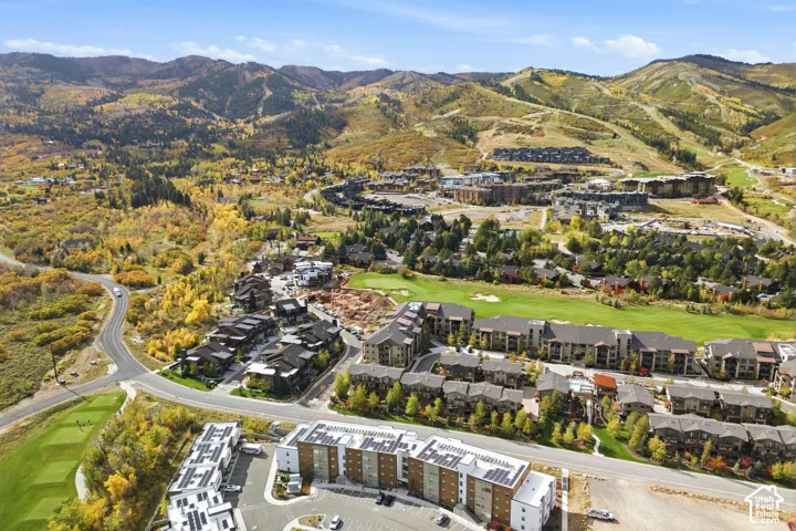 Aerial perspective featuring multi-story residential buildings with solar panels, set against a mountainous landscape with surrounding green space and paved roadways