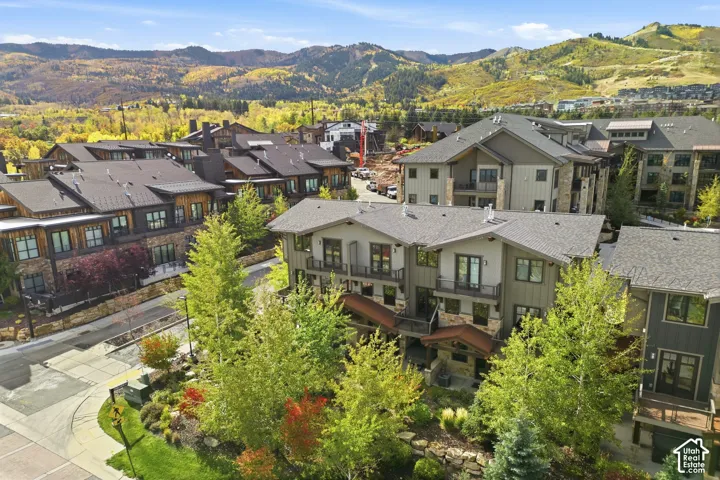 Multi-level architectural exterior featuring stone and siding construction, metal roof accents, private balconies, and surrounding mature landscaping set against a mountainous backdrop