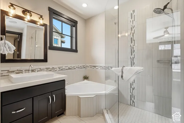 Bathroom featuring a dark-finish vanity with a rectangular vessel sink, corner soaking tub, and a glass-enclosed shower with tiled accents