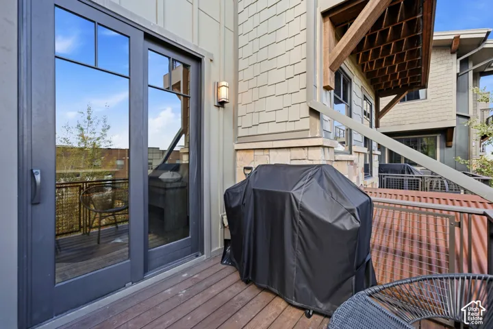 Covered outdoor deck featuring wood-finish decking, stone veneer siding, decorative timber corbels, metal railings, and dual-pane glass door entry