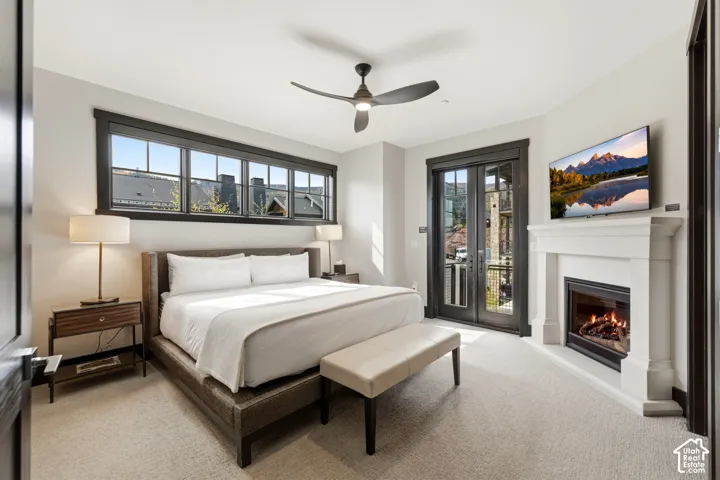 Bedroom featuring a custom fireplace with a white mantel, high-contrast dark window and door trim, multi-pane transom windows, and a ceiling fan