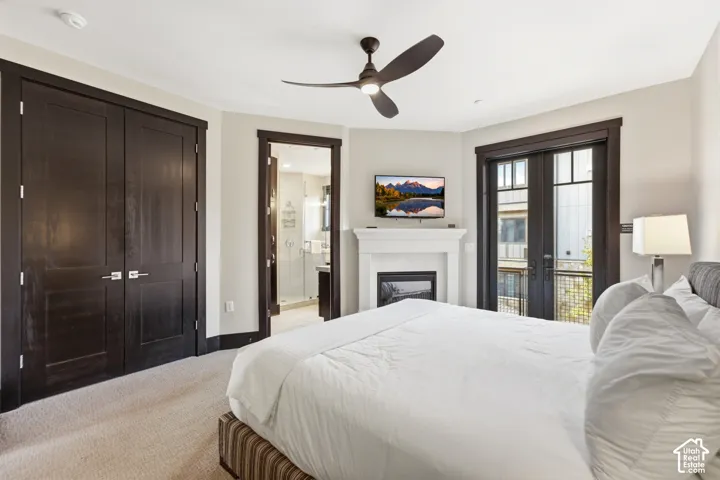 Gas fireplace with a crisp white mantel, dark-stained wood doors, multi-pane glass balcony doors, and a three-blade ceiling fan