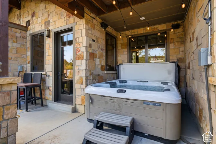 Covered patio featuring stone exterior walls, concrete flooring, and built-in overhead string lighting