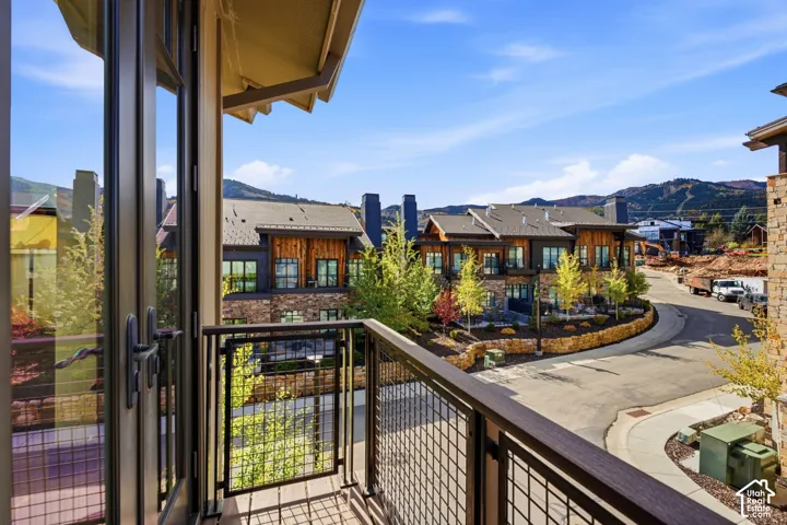 Elevated balcony featuring a dark metal wire railing and wood-tone deck, offering an overlook of the neighborhood with mountain scenery