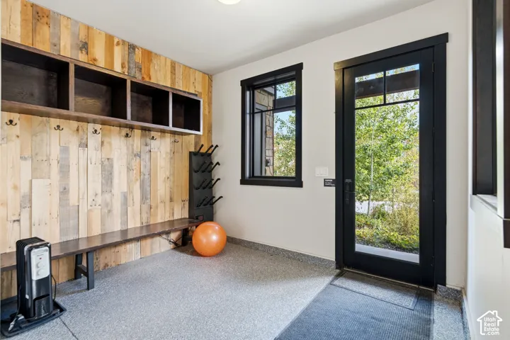 Mudroom featuring vertical wood-plank wall paneling, built-in open shelving, a bench, textured epoxy flooring, and a glass-panel exterior door with dark trim