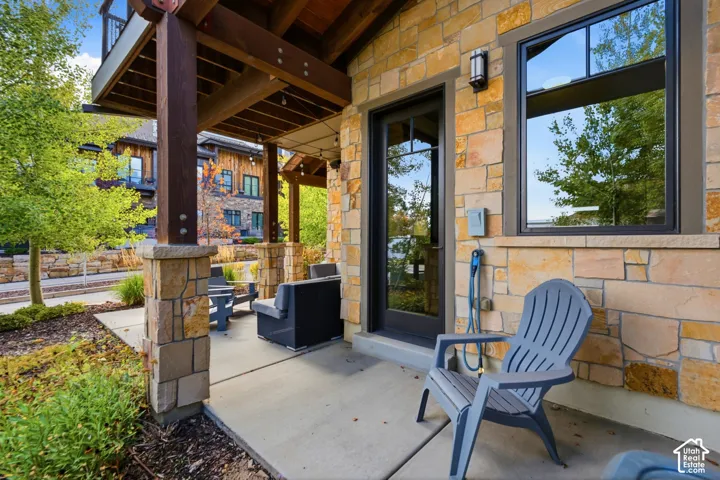Covered patio featuring stone exterior cladding, timber support beams, concrete flooring, and full-lite glass exterior door