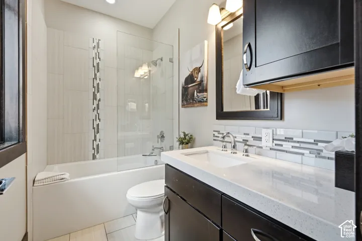 Bathroom featuring a dark-finish vanity with a light-toned countertop, tile-surround tub with glass panel, mosaic tile backsplash, and wall-mounted cabinetry