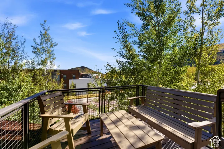 Elevated deck featuring wood-finish flooring and a metal wire railing system, framed by mature trees and mountain scenery