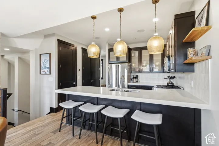 Kitchen featuring custom dark cabinetry, quartz countertops with a breakfast bar, textured tile backsplash, natural wood floating shelves, and three glass pendant lights over the island