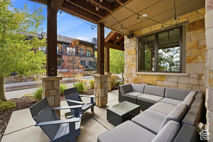Covered stone patio featuring substantial wood support columns, natural stone masonry, concrete flooring, and string lighting