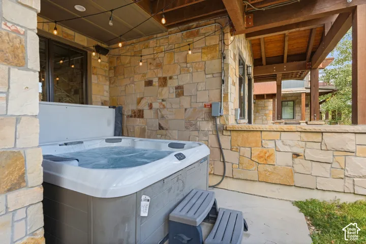 Covered outdoor patio featuring natural stone exterior walls, exposed timber beam ceiling, and a built-in spa