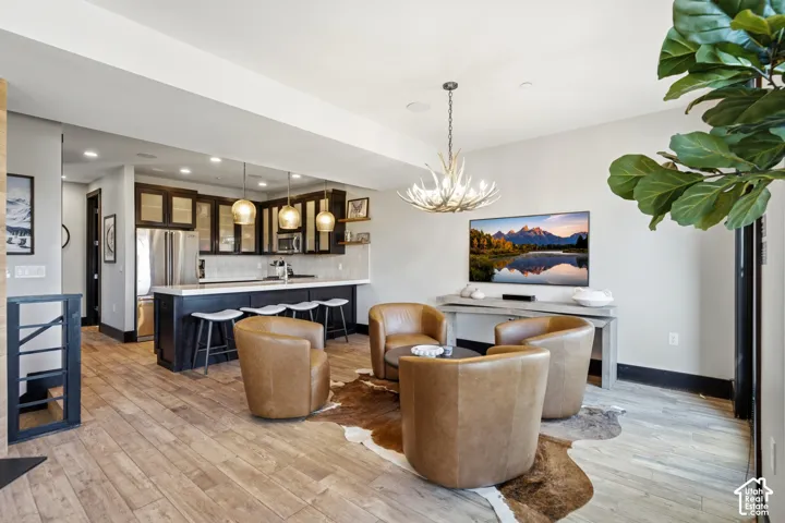 Open-concept interior featuring wood-finish flooring, a kitchen with dark cabinetry and a breakfast bar, recessed lighting, and a decorative antler chandelier
