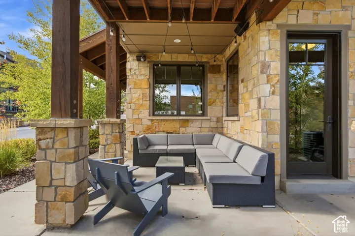 Covered patio featuring stone masonry columns, exposed timber beams, concrete flooring, and a glass-paneled exterior door
