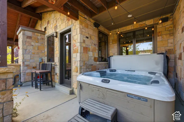 Covered patio featuring stacked stone masonry, exposed wood timber beams, a built-in spa, and concrete flooring
