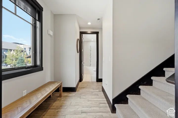 Wood-finish tile flooring, contrasting black door and window casing, built-in wooden bench, carpeted staircase with dark-finished stringer, and recessed ceiling lighting