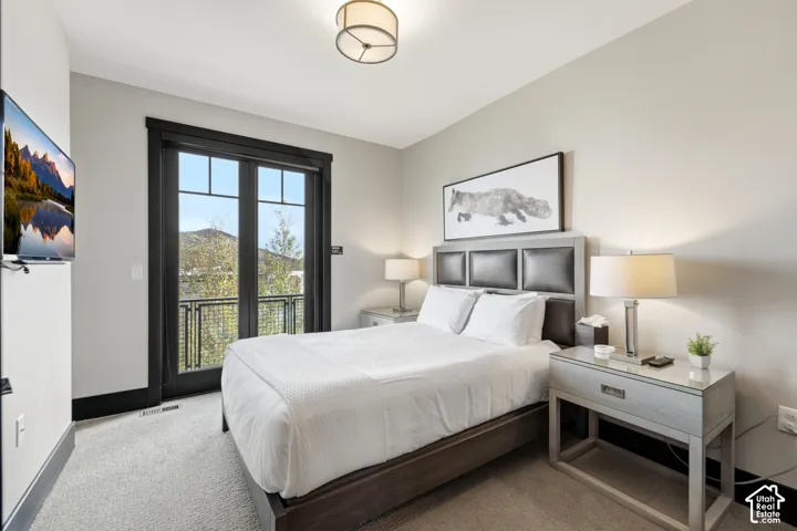 Bedroom featuring wall-to-wall carpeting, black-framed glass paneled door, metal balcony railing, and neutral wall paint