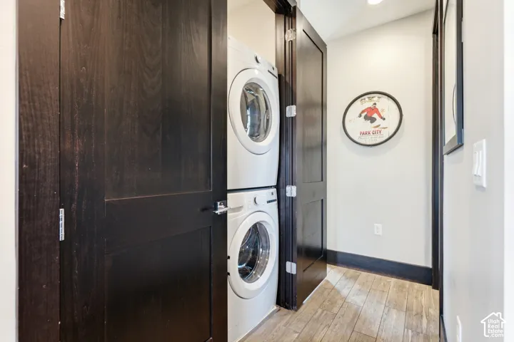 Laundry area featuring stacked appliances, dark-finish wood doors, and wood-finish flooring