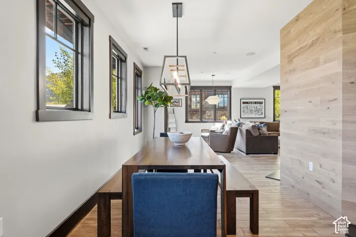 Interior featuring wood-finish flooring, accent wall with light wood paneling, multiple windows with dark frames, and a geometric pendant light fixture