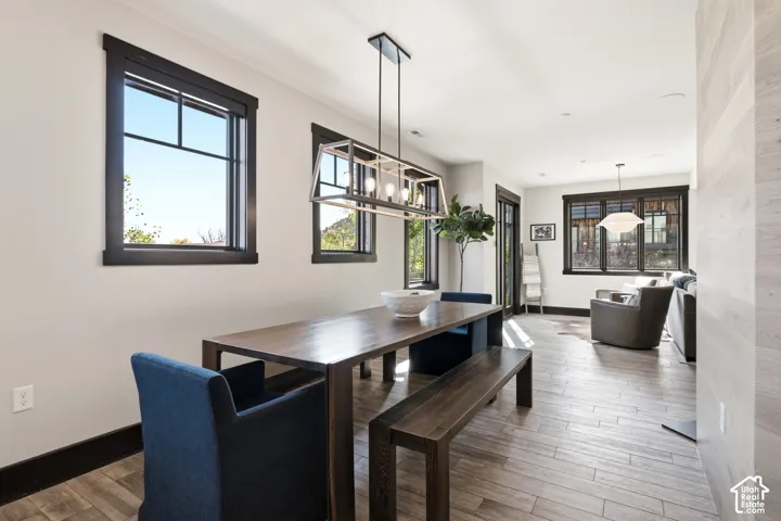 Open-concept space featuring wood-finish flooring, dark-trimmed windows, a linear multi-bulb pendant fixture, and a neutral wood-paneled feature wall