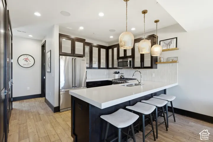 Kitchen featuring dark cabinetry with glass-panel inserts, quartz countertops, stainless steel appliances, wood-finish flooring, and pendant lighting
