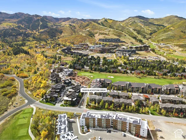 Aerial perspective featuring a multi-story residential structure located within a mountain-base landscape with proximity to golf course fairways and wooded terrain