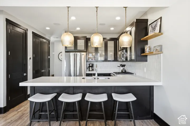 Kitchen featuring dark-finish cabinetry, quartz countertops, stainless steel appliances, tiered pendant lighting, and vertical-tile backsplash