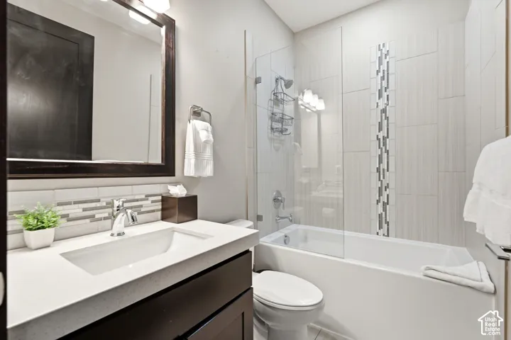 Bathroom featuring a dark-finish vanity with a light-toned countertop, integrated sink, framed mirror, and a shower-tub combination with vertical decorative tile accents and a glass panel