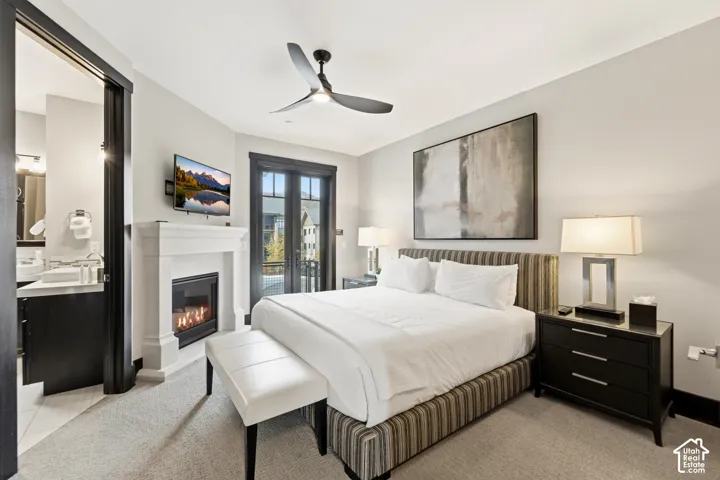 Gas fireplace with a stone-finish mantel, French doors, carpeted flooring, and a modern three-blade ceiling fan