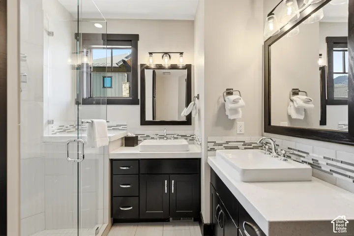 Dual vanity with rectangular vessel sinks, quartz countertops, dark-finish cabinetry, glass-enclosed walk-in shower, and mosaic tile backsplash