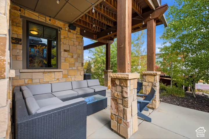 Covered patio featuring stacked stone masonry, exposed timber support beams, and a concrete floor