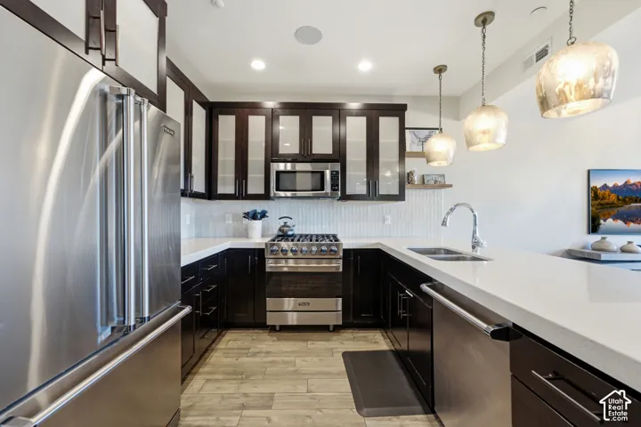 Kitchen featuring dark wood cabinetry with glass-panel upper doors, white quartz countertops, stainless steel appliances, wood-finish flooring, and trio of pendant lights