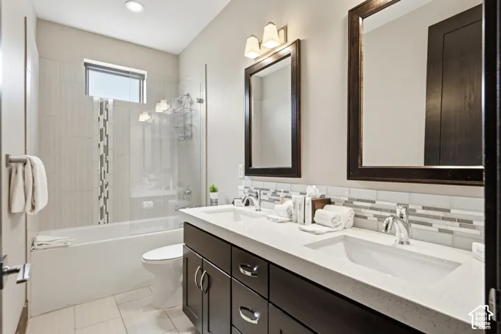 Dual-vanity cabinetry with a light-toned solid surface countertop, undermount sinks, glass-enclosed shower with mosaic tile inlay, and framed vanity mirrors