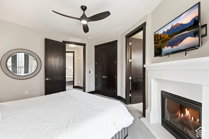 Gas fireplace with a white mantel, high-contrast dark wood doors, modern three-blade ceiling fan, and built-in circular wall mirror