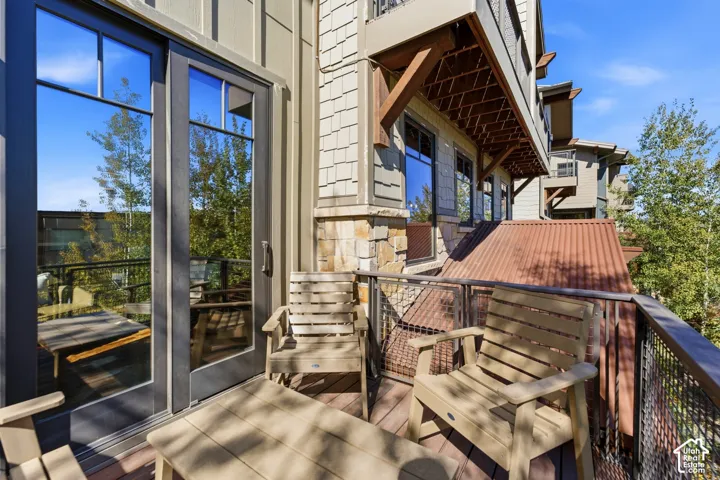 Exterior balcony featuring wood-finish decking, cable railing, stone masonry accents, shingle siding, and full-height glass door entry