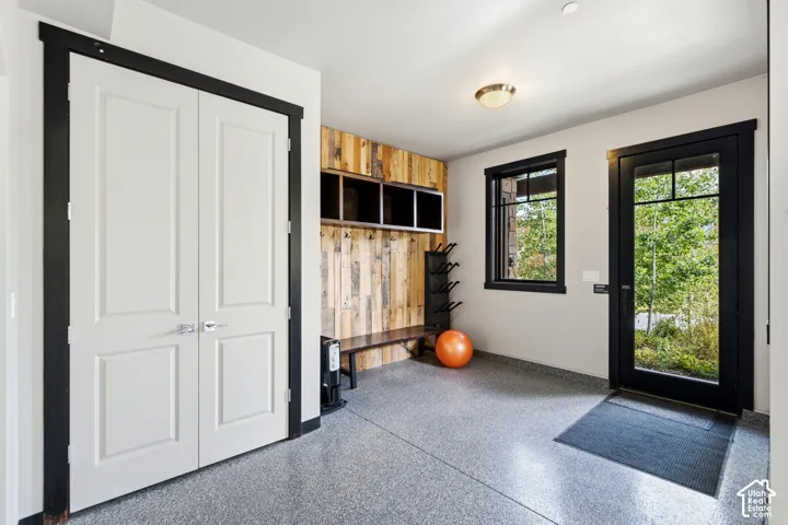 Entryway featuring epoxy flooring, built-in wooden bench with overhead storage cabinetry, solid-core double doors, and exterior door with glass panes, all accented by high-contrast black trim