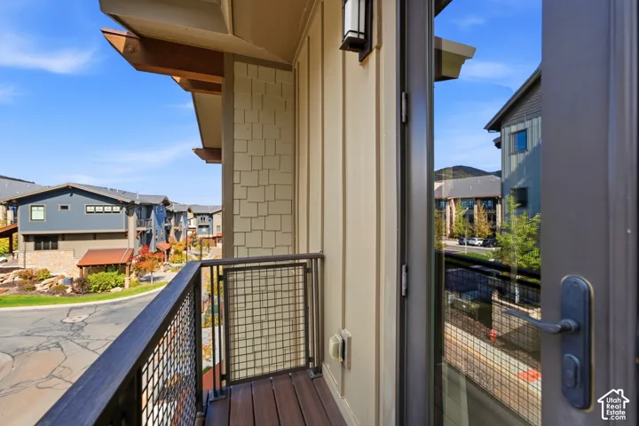 Exterior balcony featuring composite decking, metal grid railings, board-and-batten siding, decorative cedar-tone brackets, and exterior wall-mounted lighting