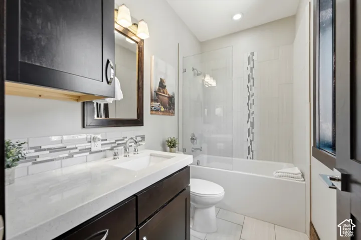 Dark wood vanity with a solid surface countertop, rectangular undermount sink, mosaic tile backsplash, and a glass-enclosed shower and tub combination