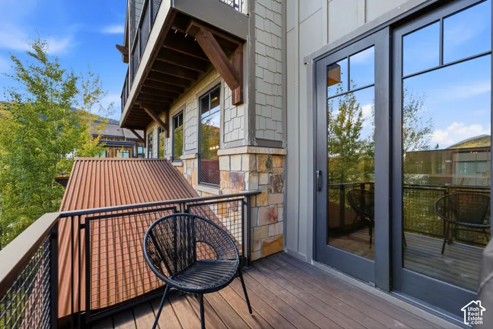 Covered balcony featuring wood decking, metal grid railings, stone veneer accents, shake siding, and glass-paneled exterior doors