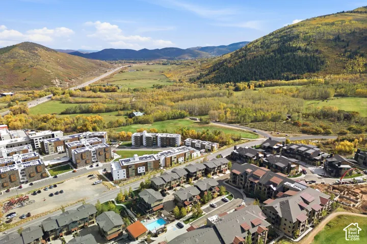 Aerial perspective of a multi-unit residential community featuring mountain terrain, natural foliage, paved roadways, and an outdoor swimming pool